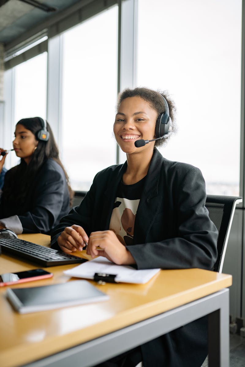 Smiling call center agent in an office setting, wearing a headset and working at a desk.